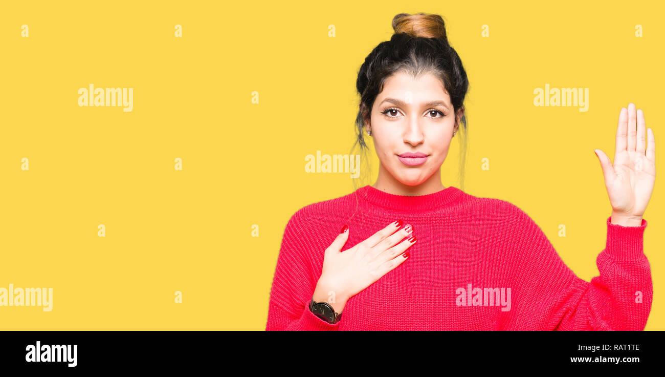Young beautiful woman wearing red sweater and bun Swearing with hand on chest and open palm, making a loyalty promise oath Stock Photo