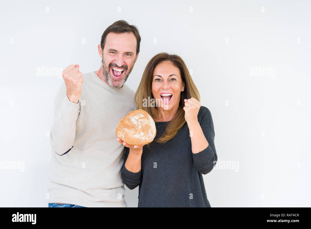 Middle age couple holding homemade fresh bread over isolated background screaming proud and celebrating victory and success very excited, cheering emo Stock Photo