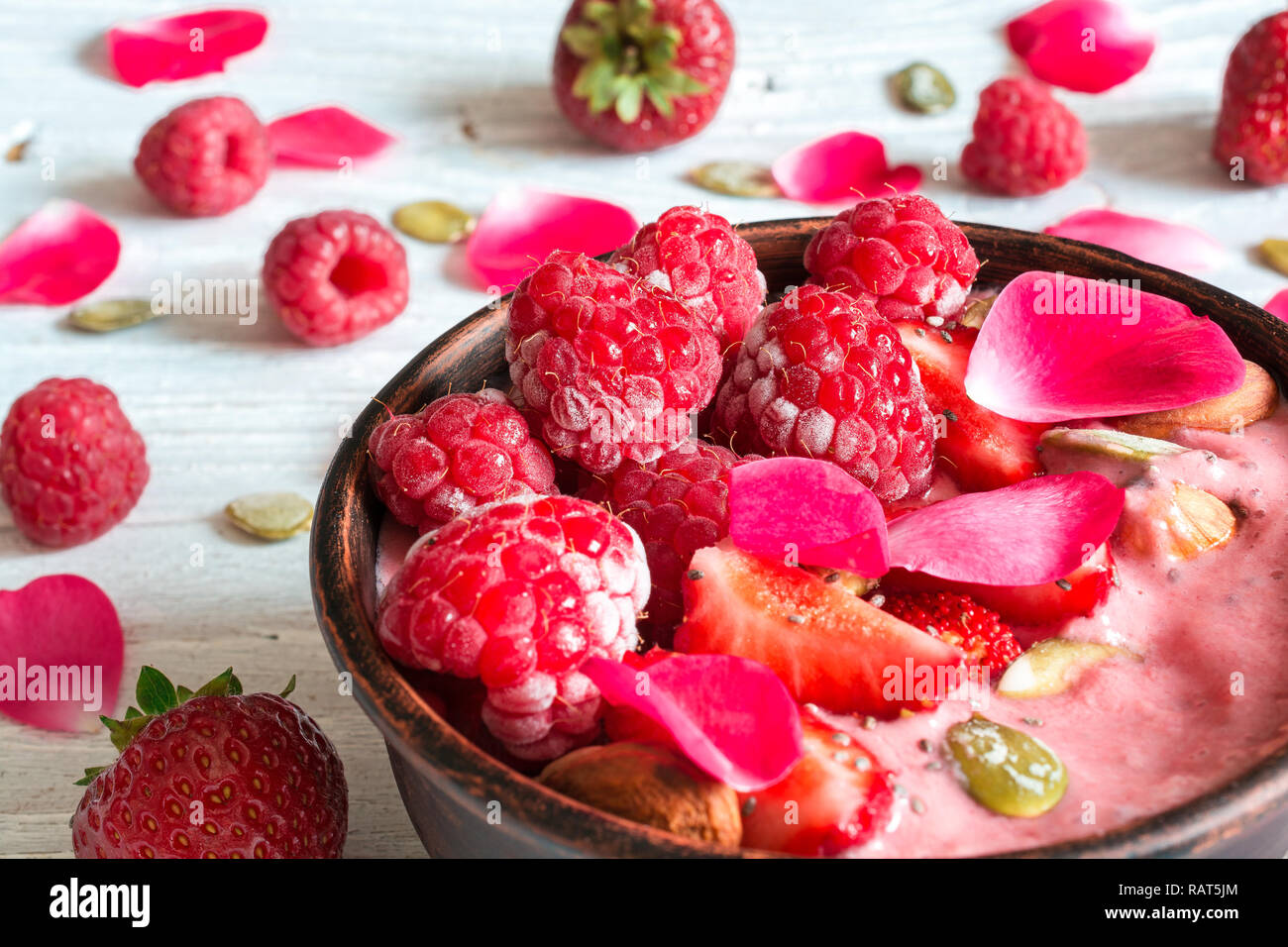 healthy breakfast. bowl of red berry smoothie with strawberry, raspberry, nuts and seeds decorated with rose flower petals. close up Stock Photo