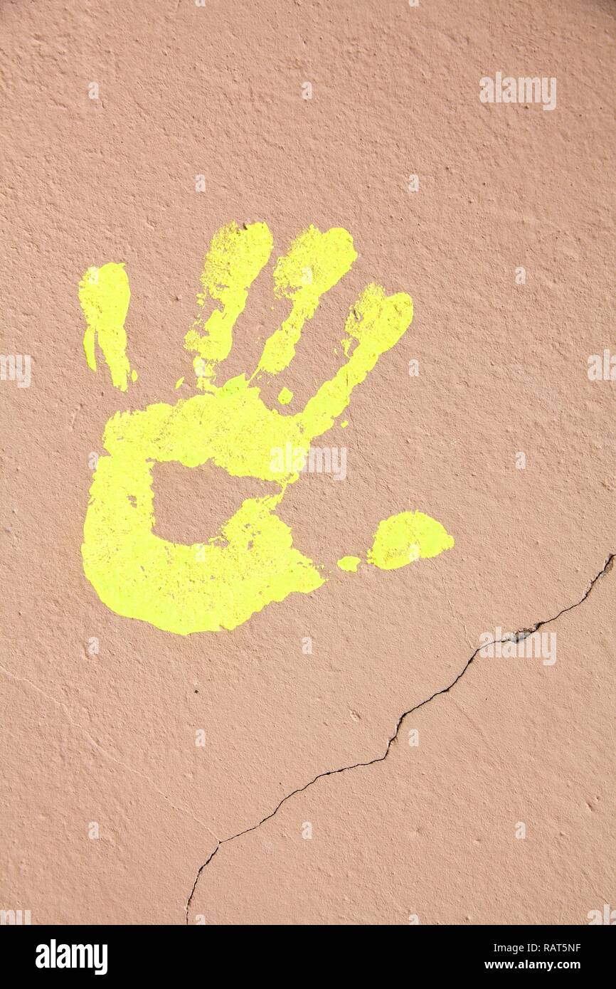 Yellow hand print on a cracked wall. Painted hand shape. Stock Photo