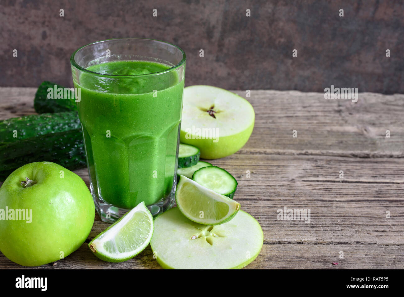 green healthy smoothie in a glass with spinach, apple, cucumber and lime over rustic wooden table. detox drink. close up Stock Photo