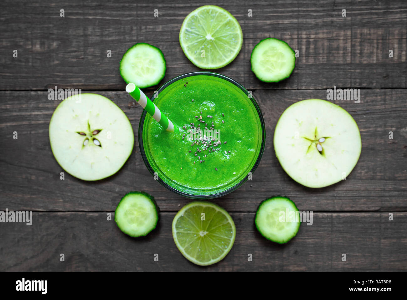 green healthy smoothie in a glass with spinach, apple, cucumber and lime with a straw over rustic wooden table. top view. detox drink Stock Photo