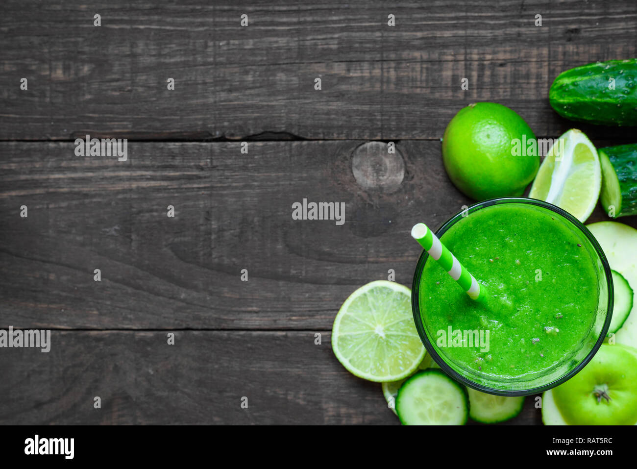 green healthy smoothie in a glass with spinach, apple, cucumber and lime with a straw over rustic wooden table. top view with copy space. detox drink Stock Photo