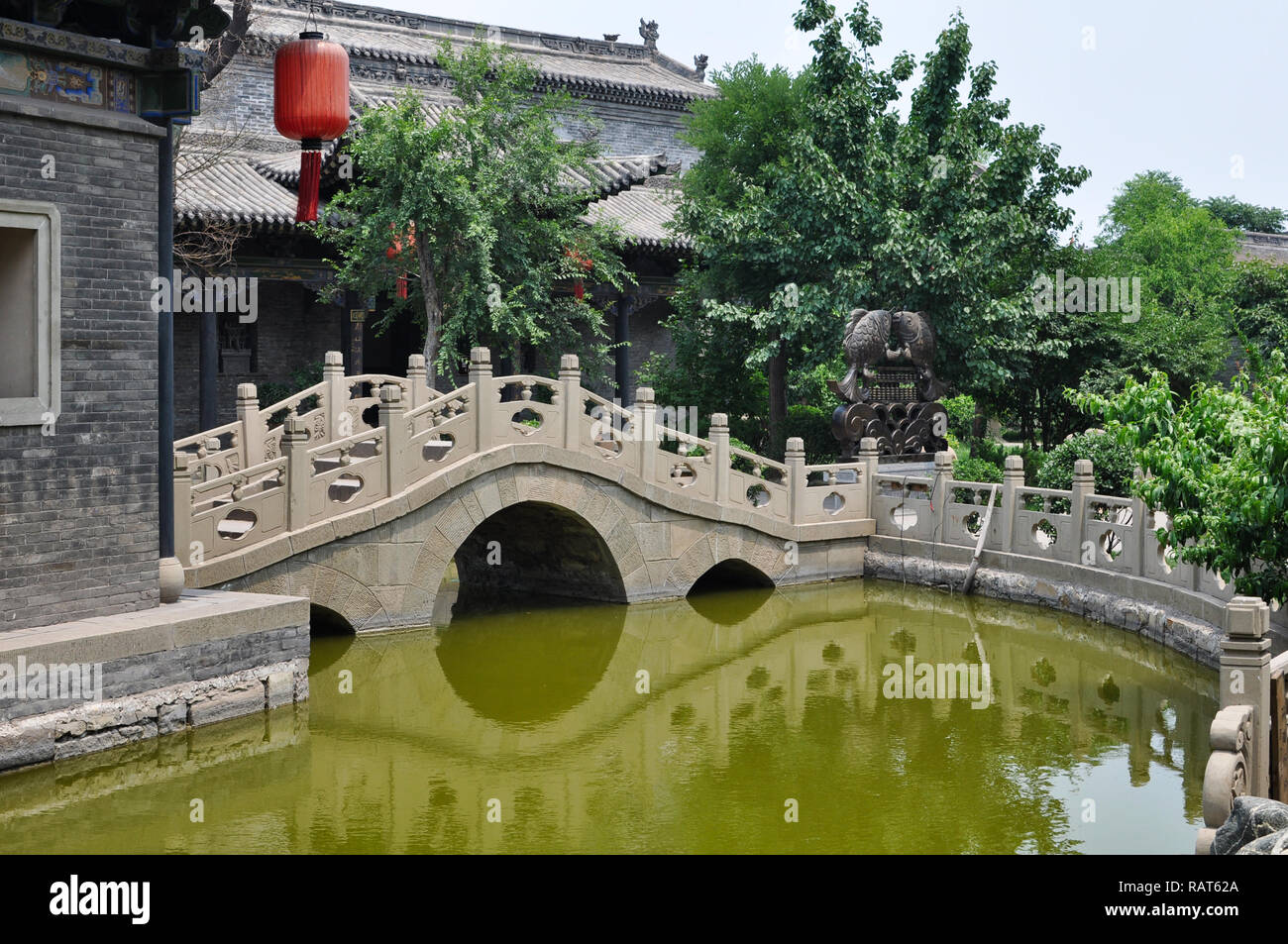 Bridge over a pond in a courtyard with trees and fishes sculpture in Pingyao, Shanxi, China Stock Photo