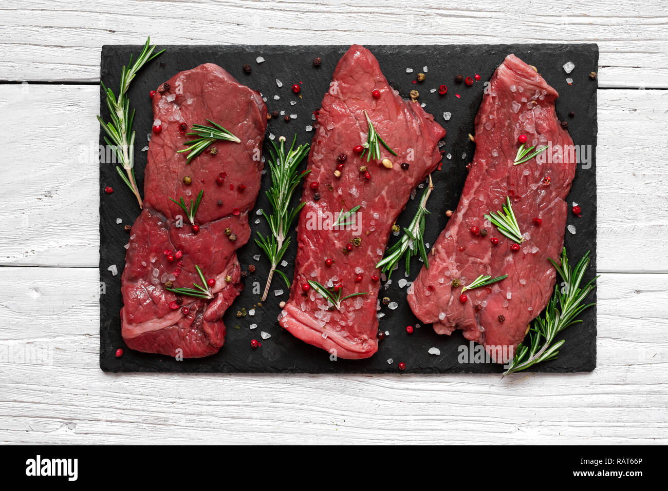 Raw meat, beef steak with spices and rosemary on black slate cutting board over wooden background. top view Stock Photo