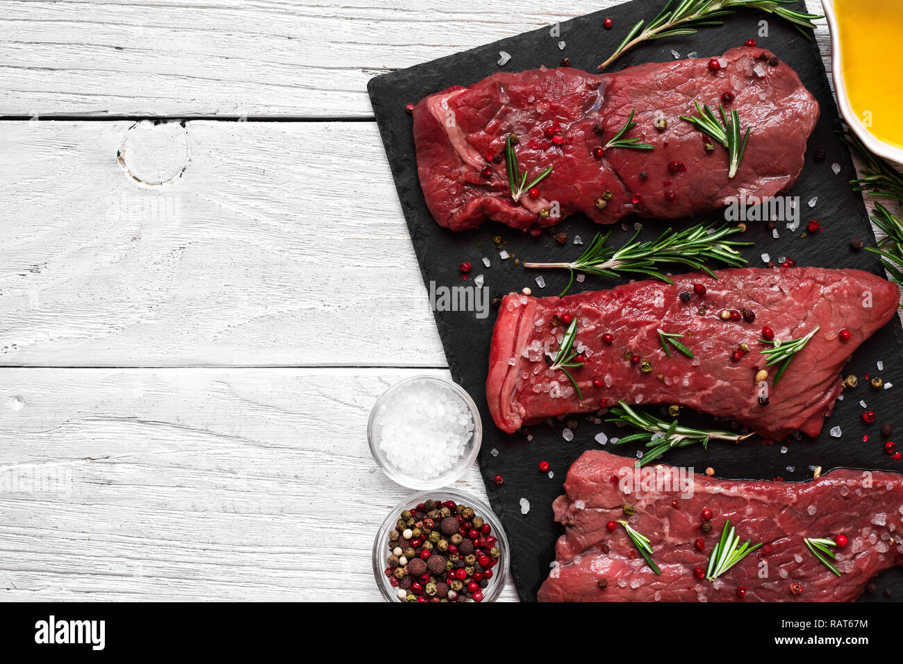 Raw meat, beef steak with spices, olive oil and rosemary on black slate cutting board over wooden background. top view with copy space Stock Photo