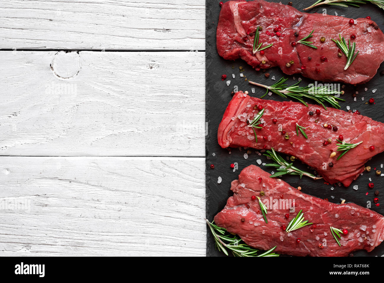 Raw meat, beef steak with spices and rosemary on black slate cutting board over wooden background. top view with copy space Stock Photo