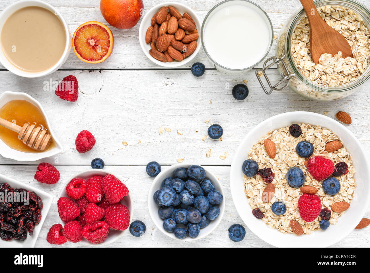 food frame made of breakfast ingredient. muesli, fruits, berries, cappuccino, nony, milk and nuts on white wooden table. healthy food. top view with c Stock Photo