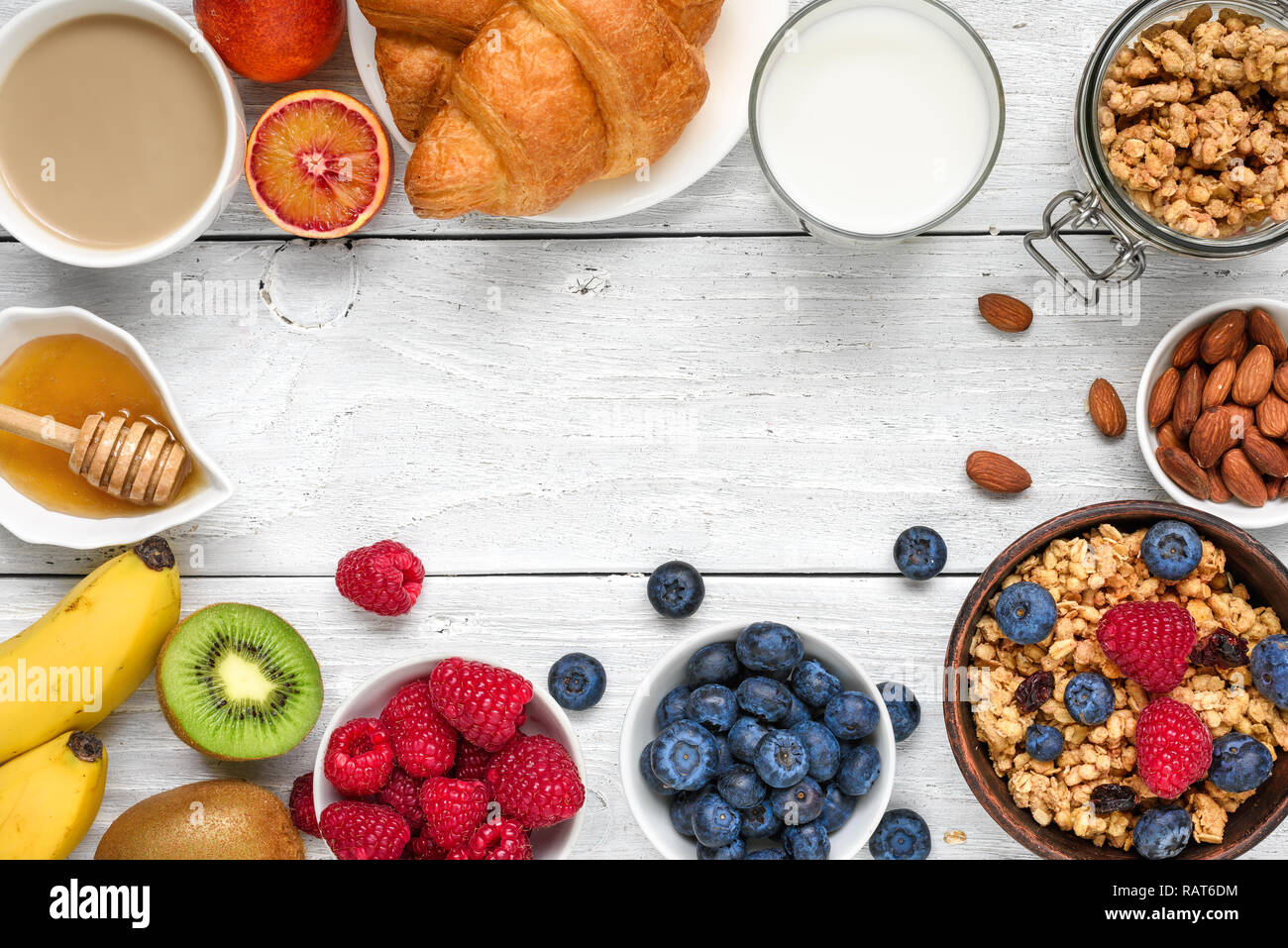 Healthy breakfast with granola muesli, fruits, berries, nuts, croissant and cup of coffee on white wooden background. top view with copy space Stock Photo