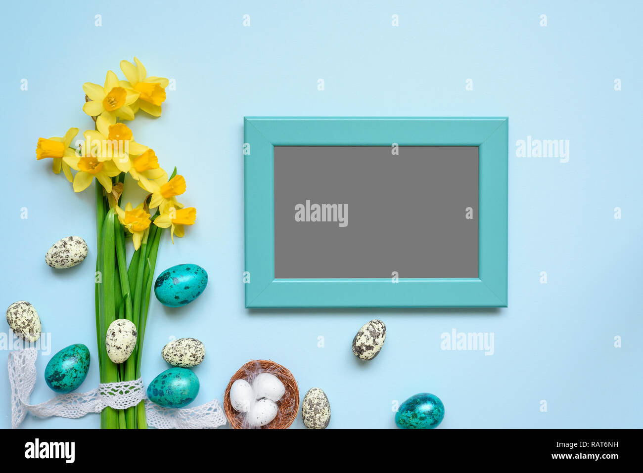 blank photo frame with easter eggs and spring flowers mock up over blue background. top view. flat lay Stock Photo