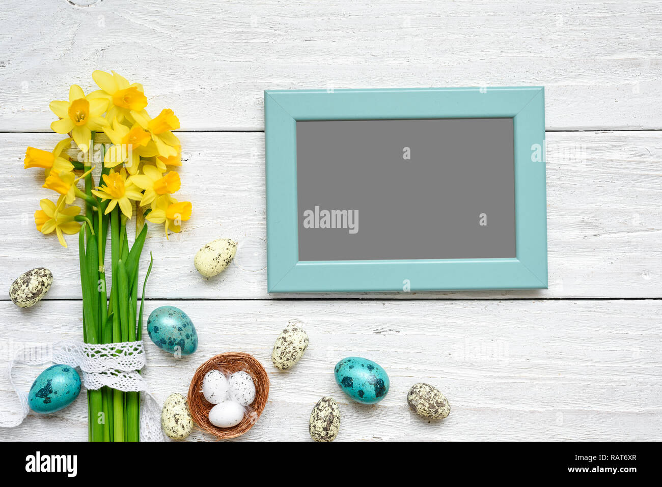 blank photo frame with easter eggs and spring flowers mock up over white wooden table. top view. flat lay Stock Photo