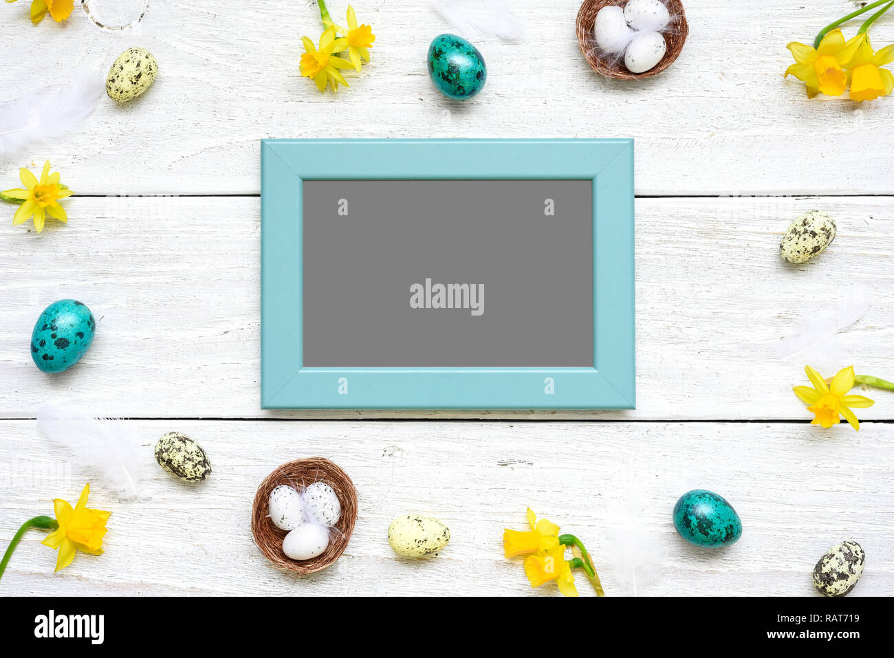 blank photo card in frame made of quail eggs, spring flowers and feathers on white wooden background. easter composition. top view with copy space Stock Photo