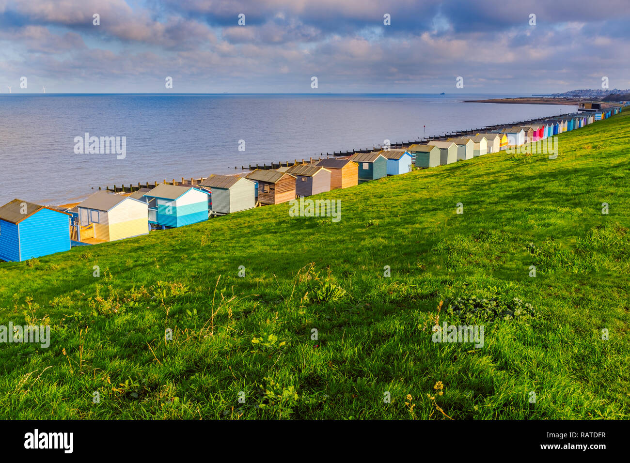 Row of beach huts along the coast in Tankerton, Whitstable, Kent. The green grass slopes are behind the huts and groynes, water breakers can be seen a Stock Photo