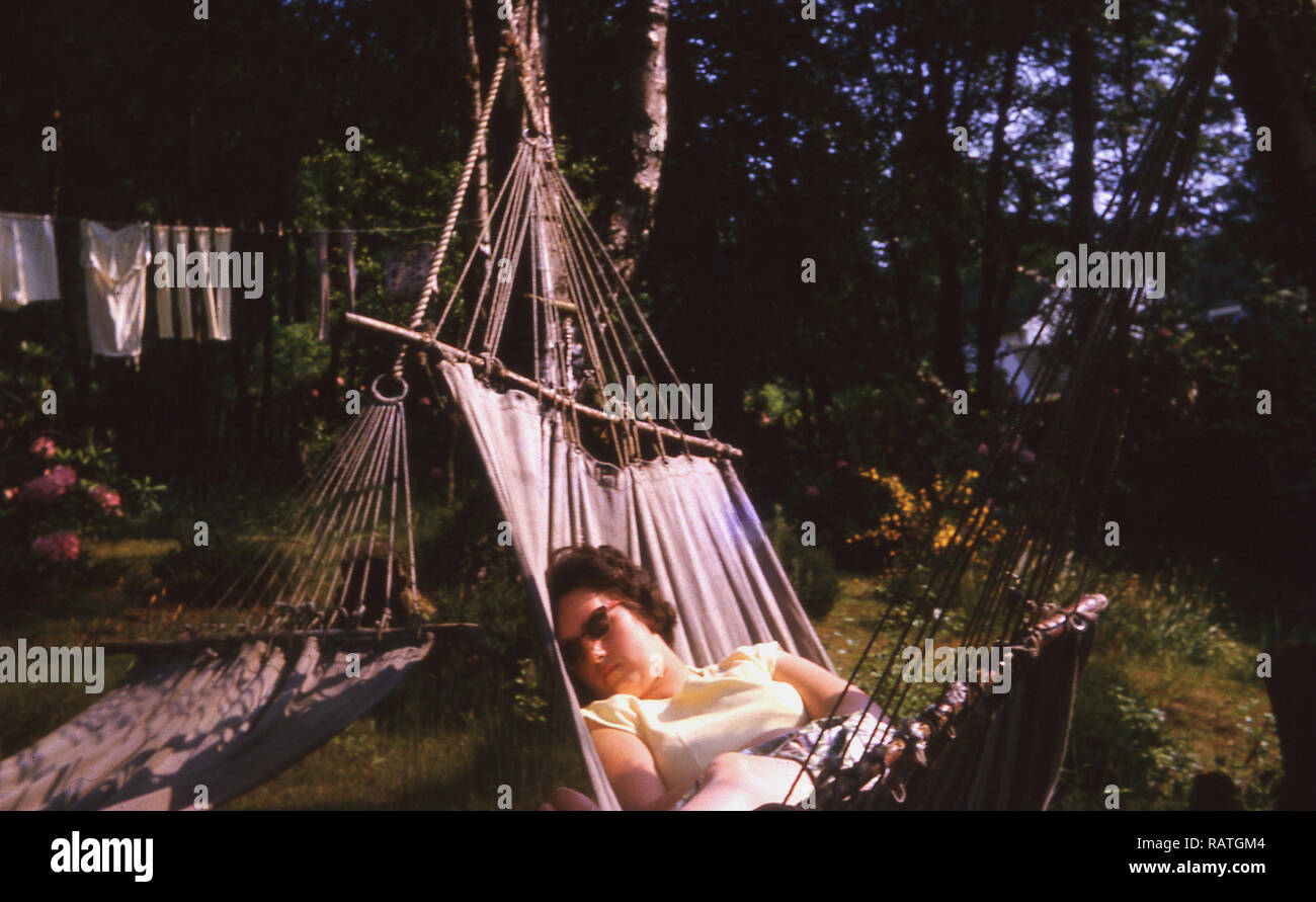 1960s, summertime and  a lady asleep on a canvas hammock outside in a garden having an afternoon nap, England, UK. Stock Photo