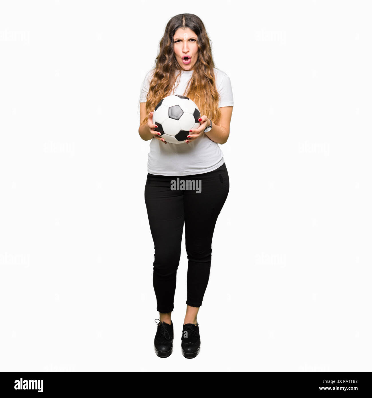 Young adult woman holding soccer football ball scared in shock with a surprise face, afraid and excited with fear expression Stock Photo