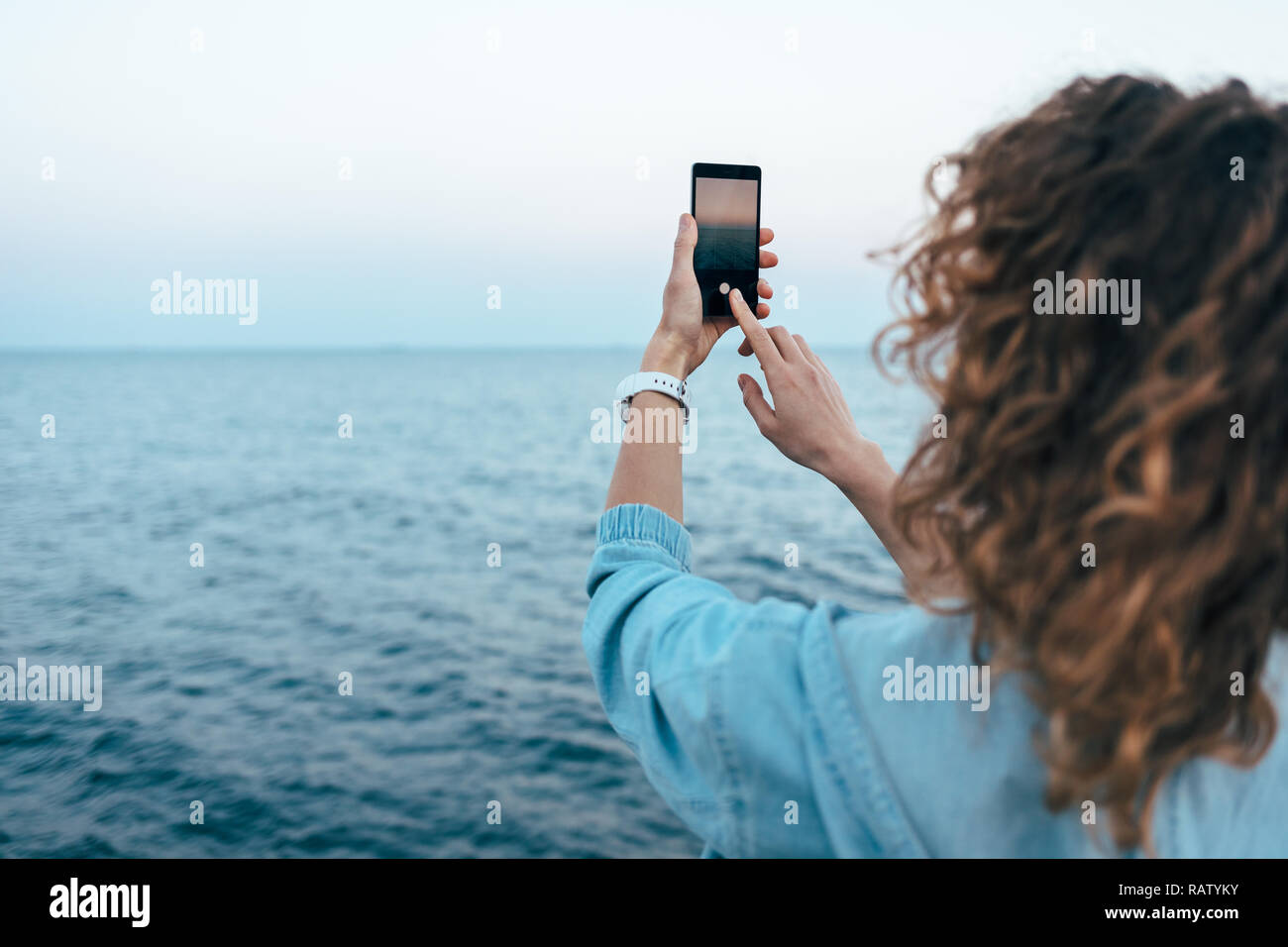 Rear view candid image young woman taking photo of blue sea on mobile
