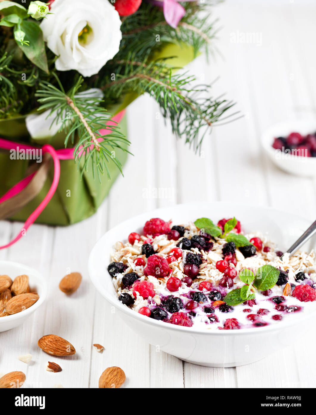 Bowl with oats, berries and almond near winter flower bouquet on wooden white background Stock Photo