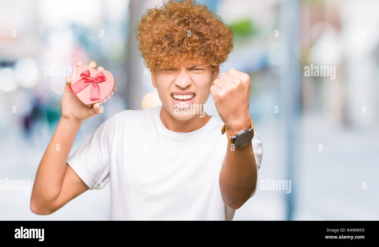Man Raging Out Gift Young handsome man holding heart box as gift of valentine's day annoyed ...