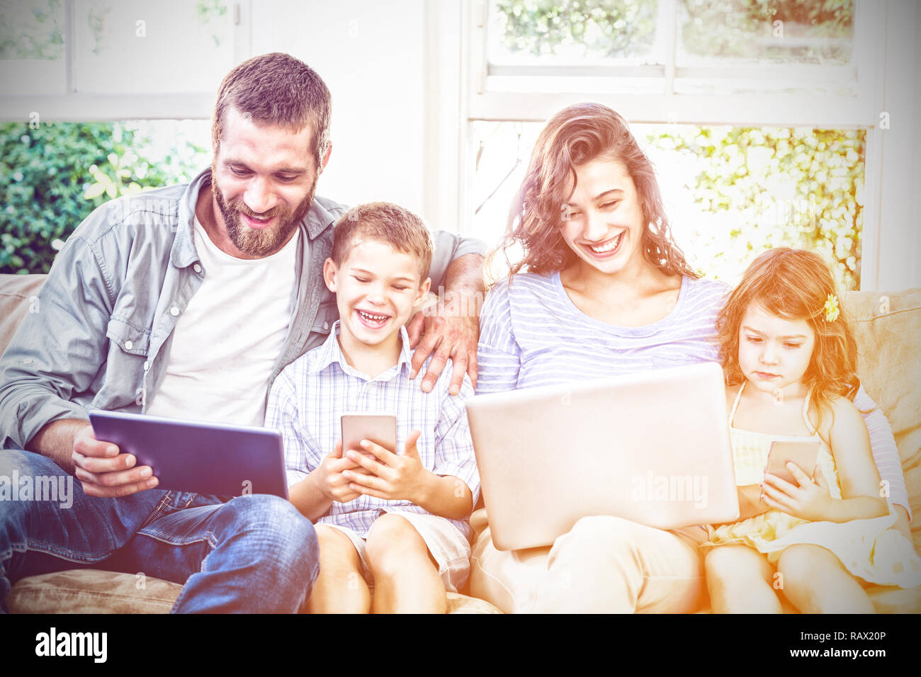 Family using technologies while sitting on sofa Stock Photo