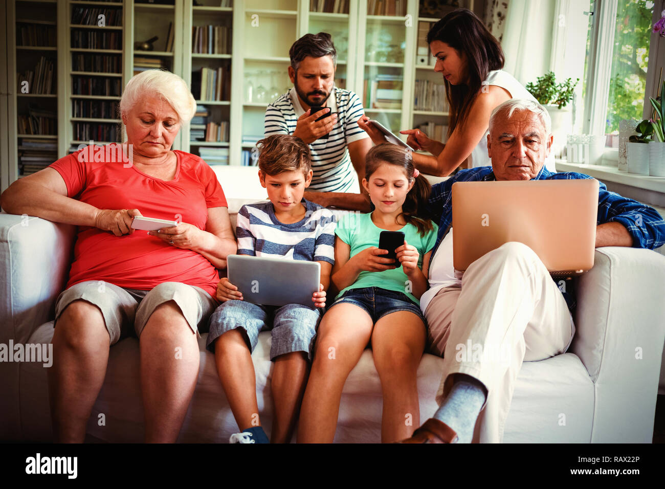 Multi-generation family sitting on sofa and using various technologies Stock Photo