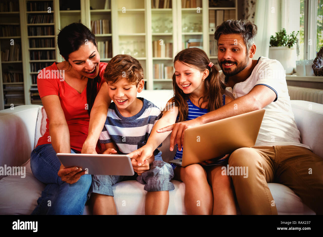 Cheerful family using technologies while sitting on sofa Stock Photo
