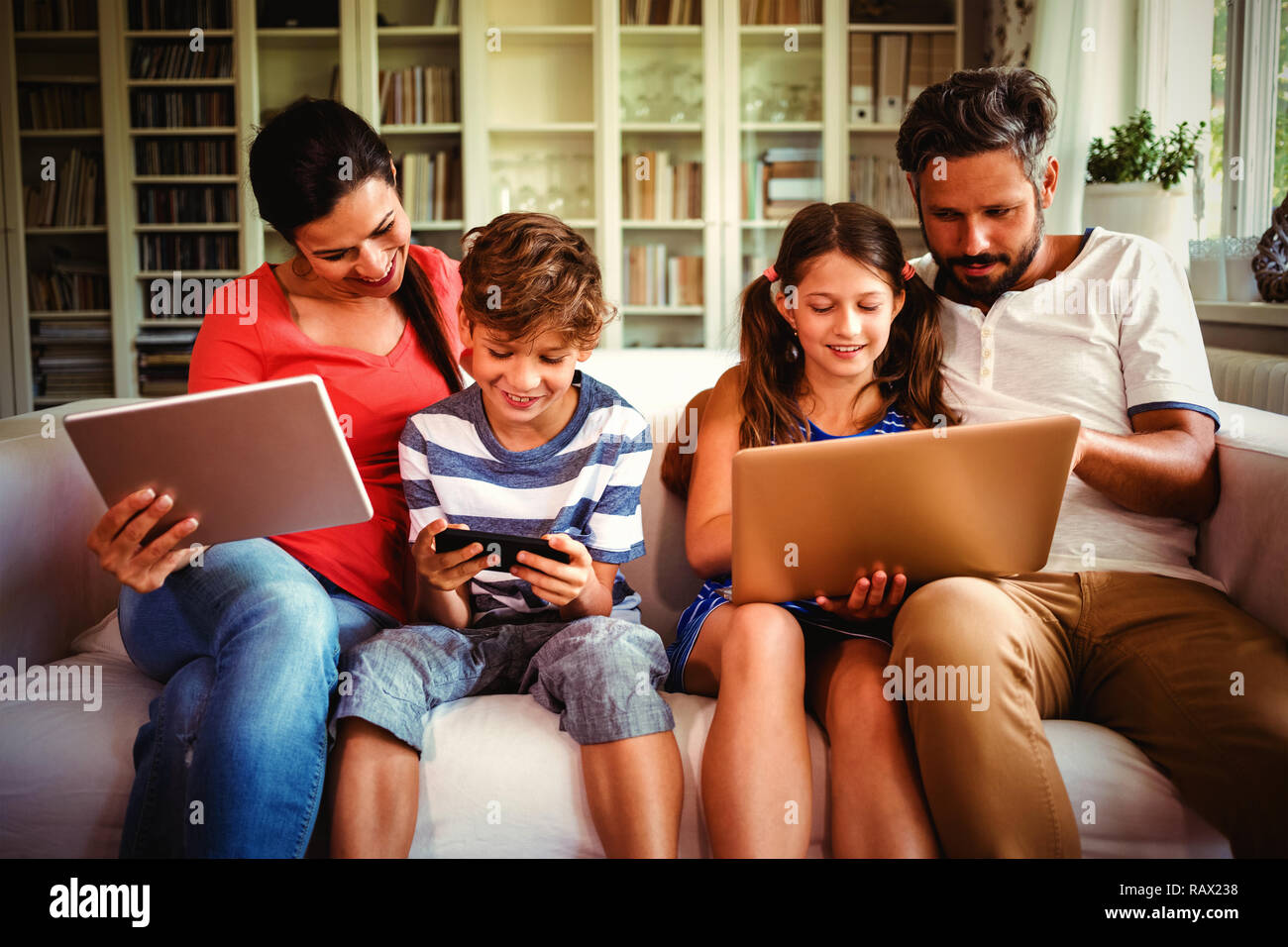 Family using various technologies while sitting on sofa Stock Photo