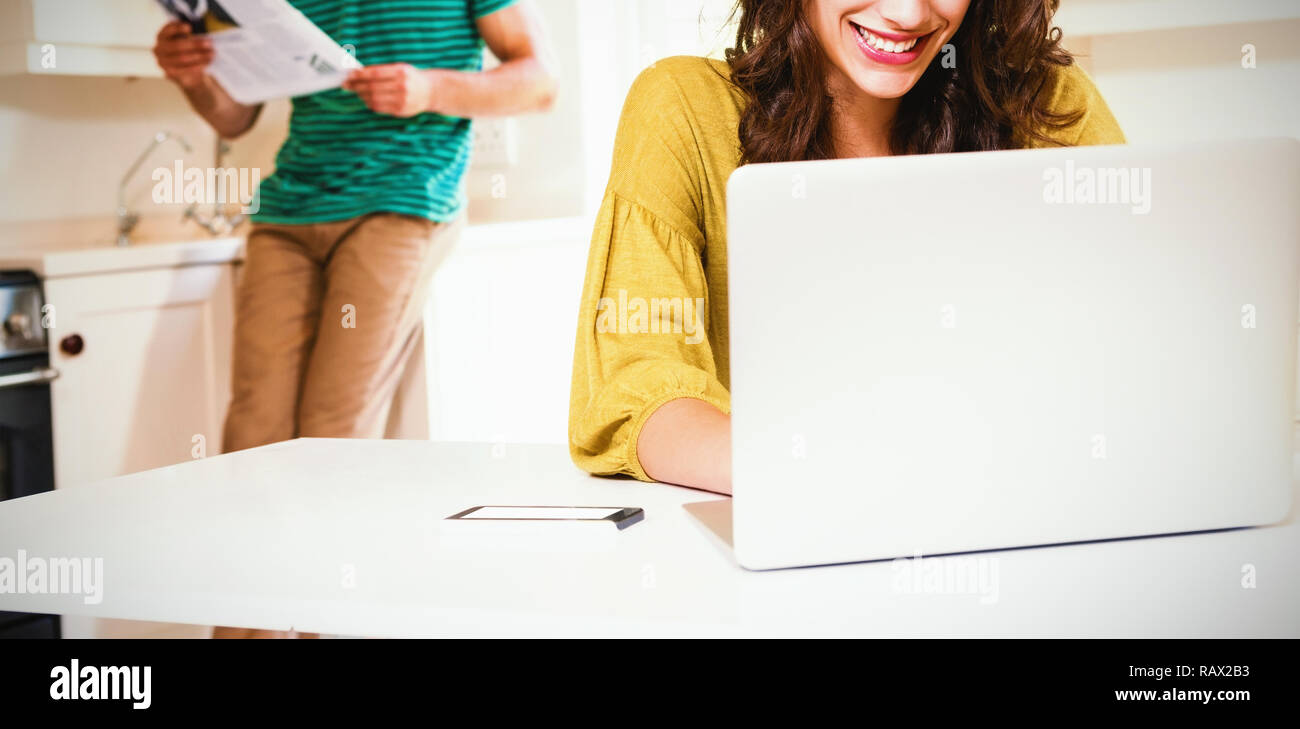 Woman using laptop while man reading newspaper in background Stock Photo