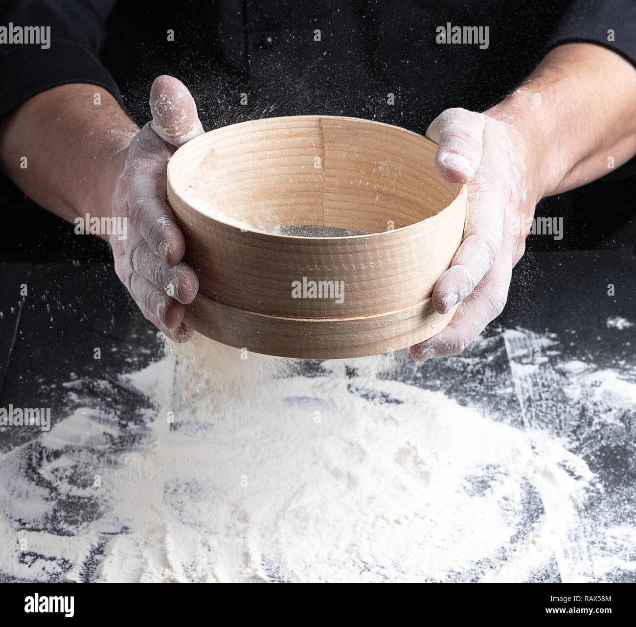 https://c8.alamy.com/comp/RAX58M/chef-in-a-black-uniform-holds-in-his-hand-a-round-wooden-sieve-and-sift-white-wheat-flour-RAX58M.jpg
