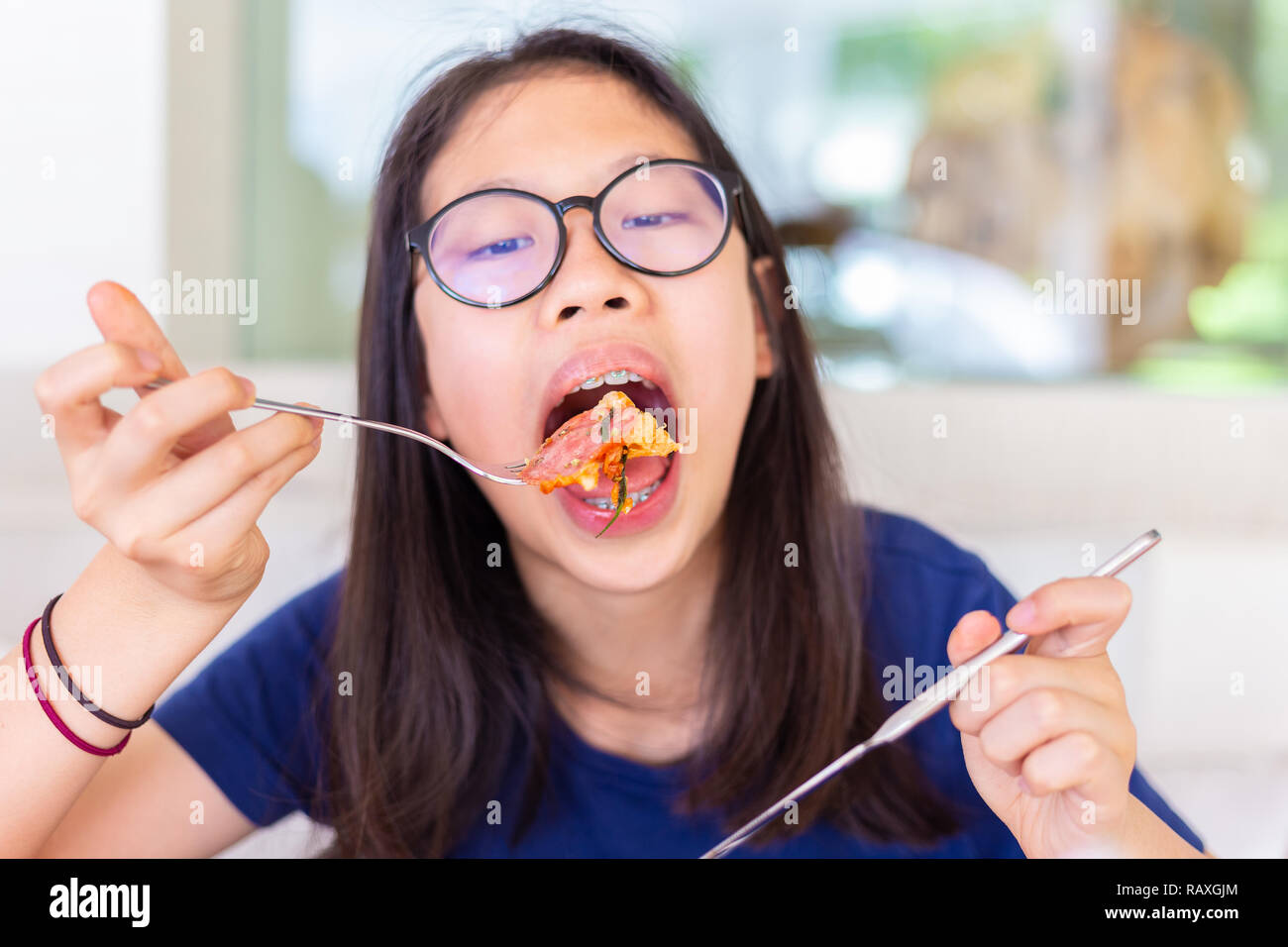 Young female teenager eating her pepperoni pizza for lunch at restaurant using fork and knife, good for health concept Stock Photo
