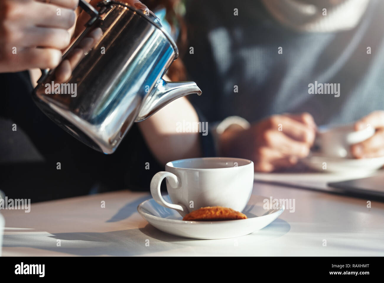 Metal teapot, cup and oat cookie on foreground. People are on background Stock Photo