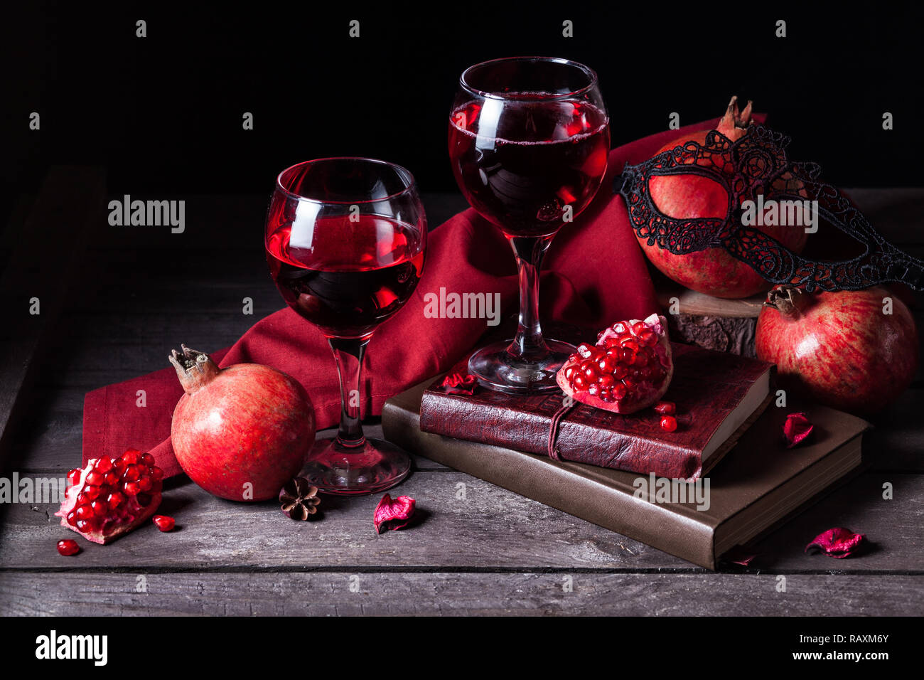 Fresh pomegranate juice in wine glasses near fruits, books and black woman mask on rustic wooden background with space for text Stock Photo