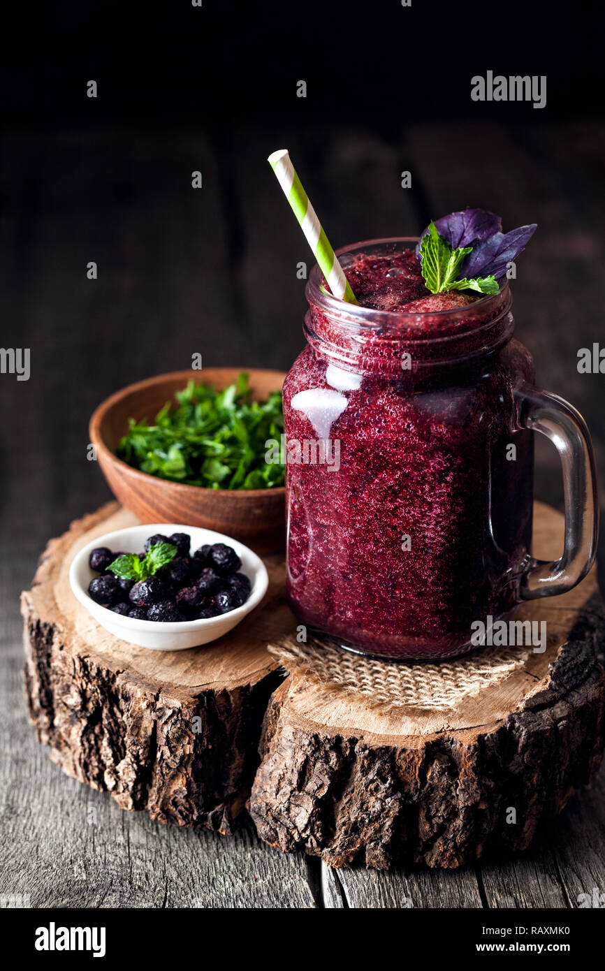 Purple smoothie with blackberry, basil, mint, dill and parsley on wooden rustic background Stock Photo