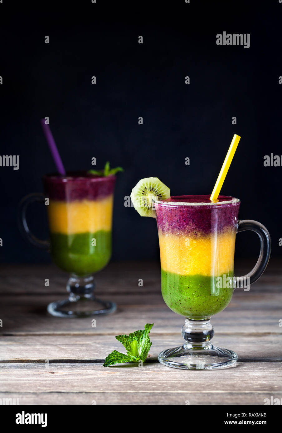Two smoothie with colorful layers from kiwi, oranges and blackberry on wooden background Stock Photo