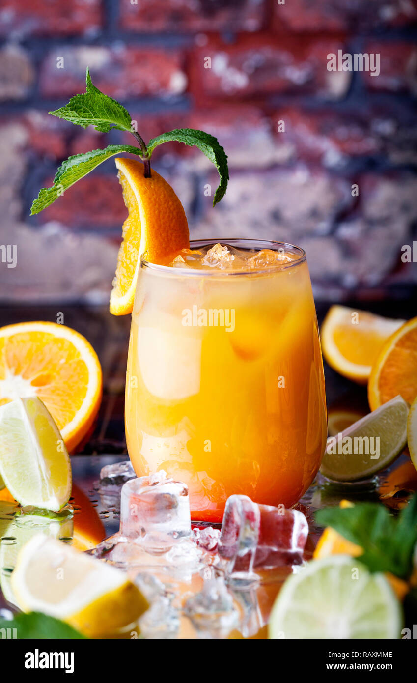 Orange cocktail with ice cubes in the tropical bar at brick wall background Stock Photo