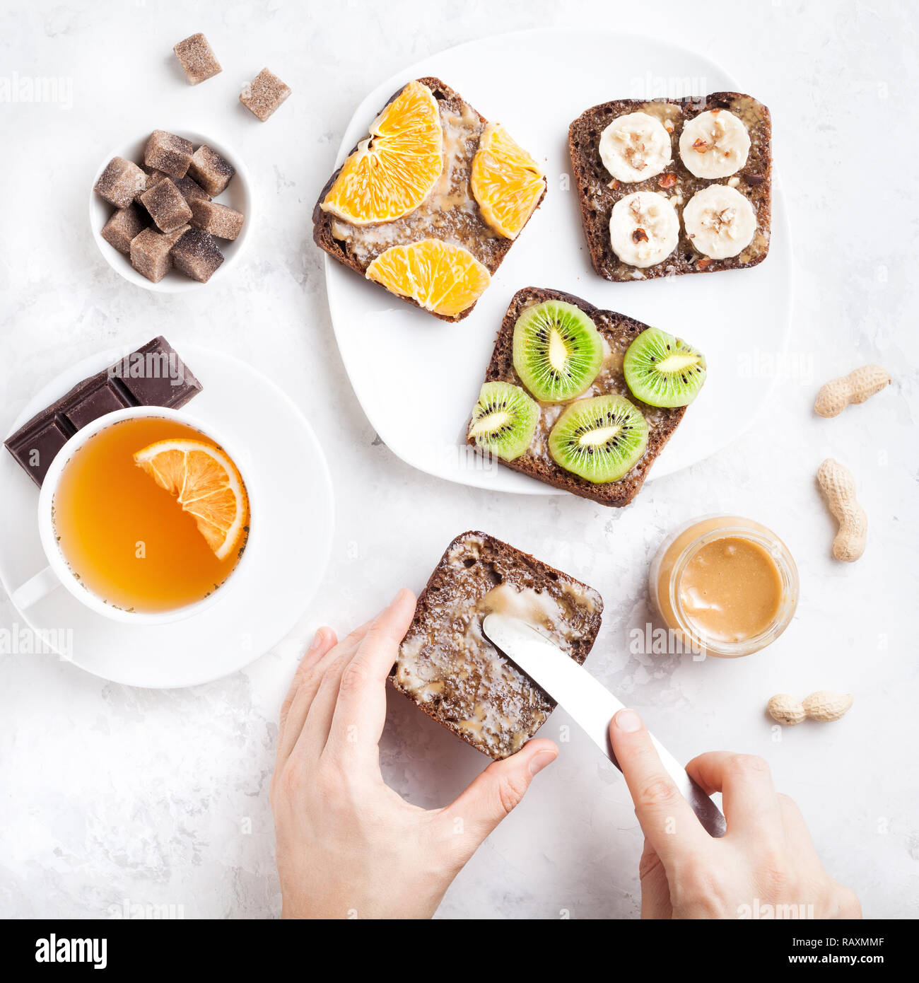 Woman hands spreading peanut butter on the bread in the morning on white marble background Stock Photo