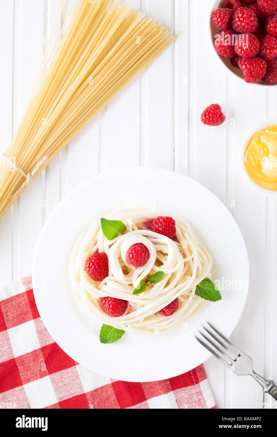 Vegetarian spaghetti with raspberry, honey and cream on white table in restaurant Stock Photo