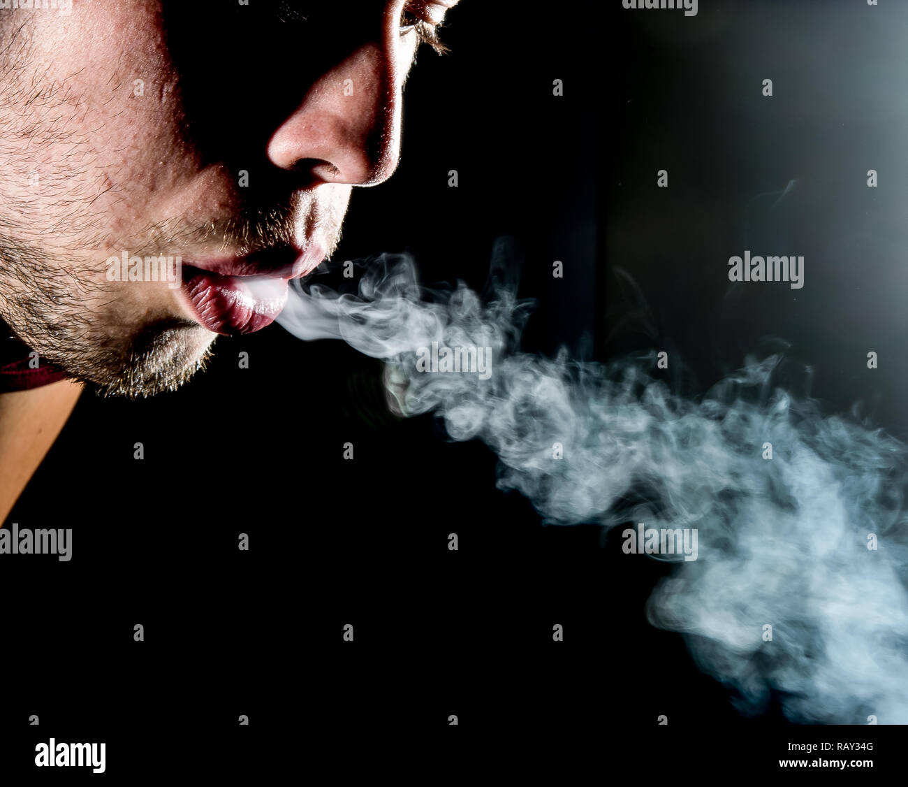 part of mans face blowing cigarette smoke out of his mouth Stock Photo