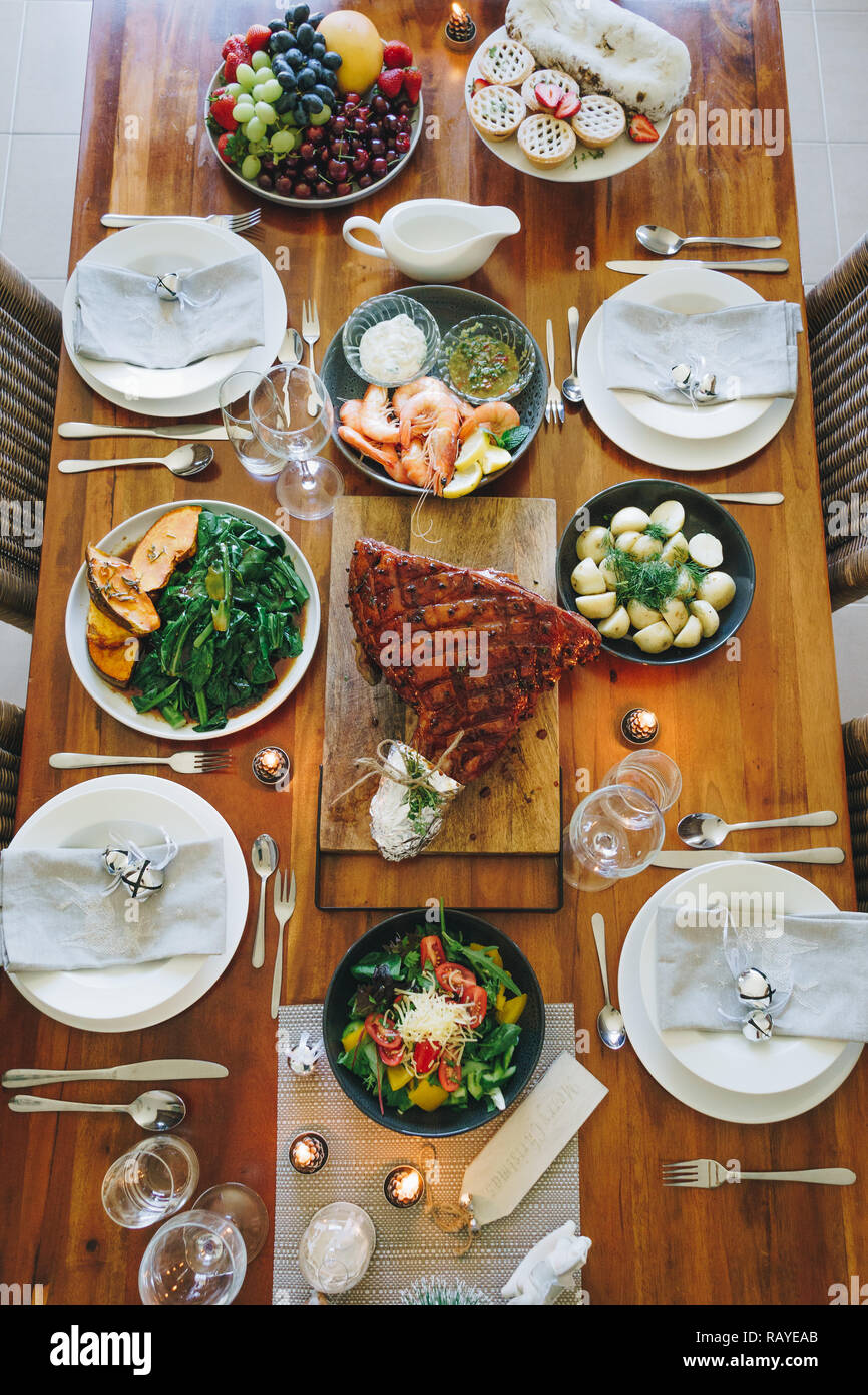 Modern Australian Christmas dinner table with glazed ham, prawns, potatoes and dill, asian greens, Christmas pudding, minced fruit pies by candlelight Stock Photo