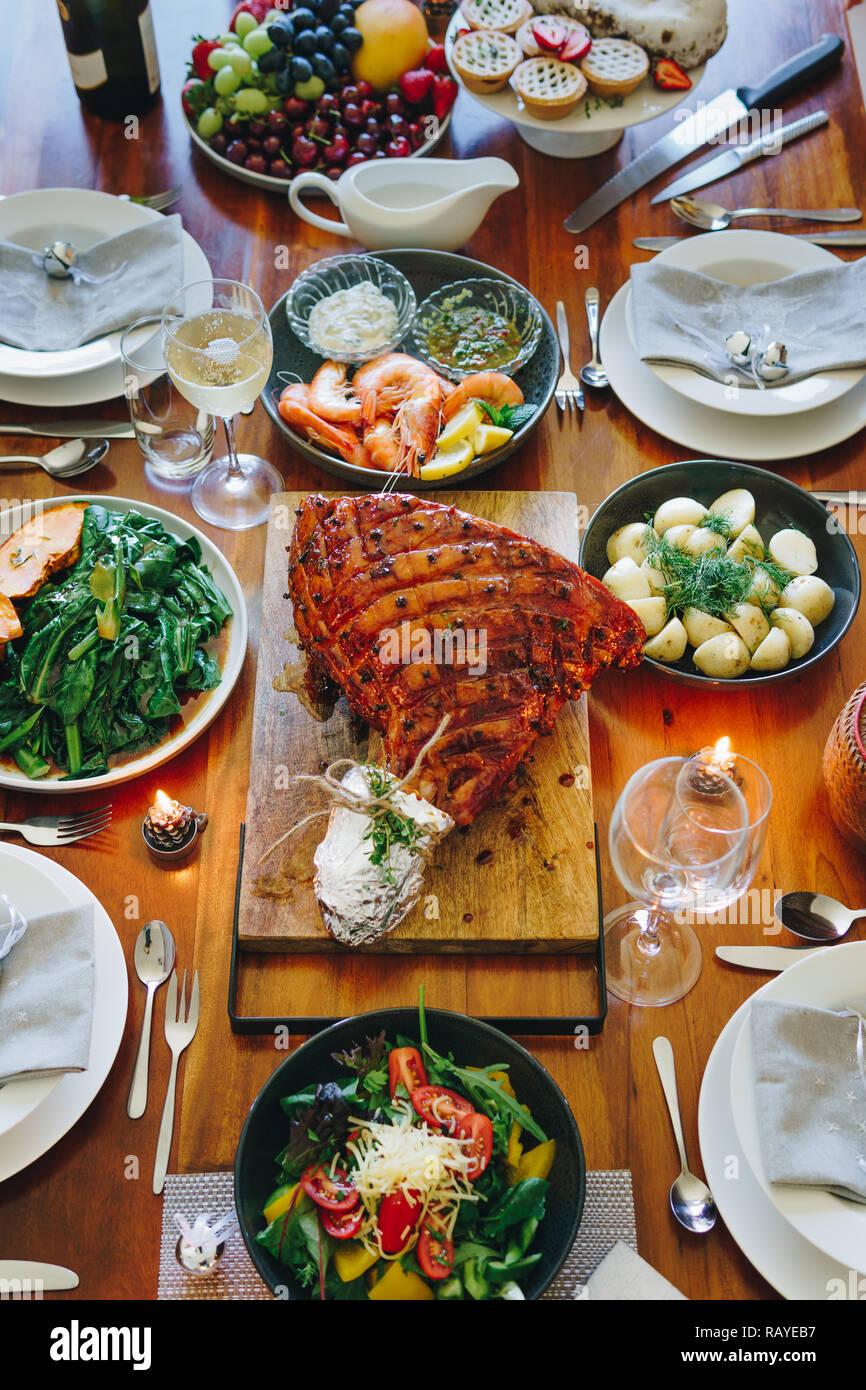 Modern Australian Christmas dinner table with glazed ham, prawns, potatoes and dill, asian greens, Christmas pudding, minced fruit pies by candlelight Stock Photo