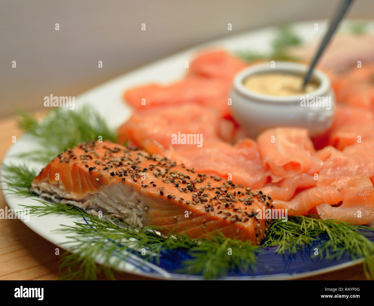 Fried salmon fillet arranged on a plate with dill, slices of smoked salmon, and a small china dish with mustard sauce Stock Photo
