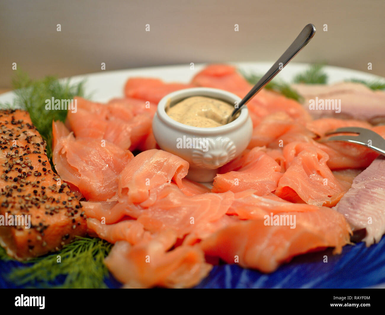 Slices of smoked salmon arranged on a plate with fried salmon fillet, dill and a small china dish with mustard sauce Stock Photo