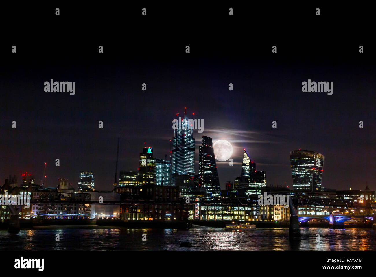 A very large moon rises from behind the towers of the City of London in an unusual display Stock Photo