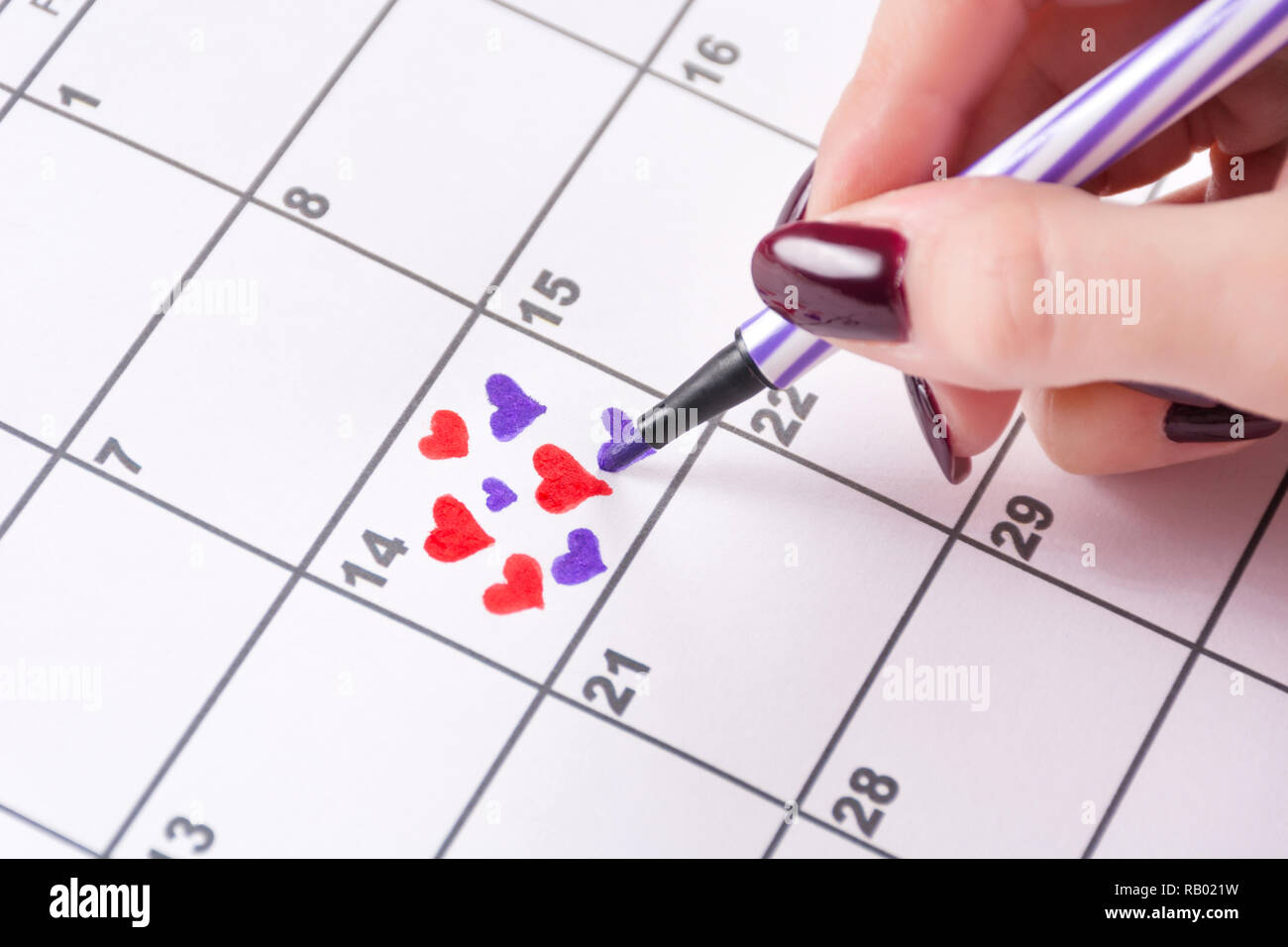 Girl hand drawing hearts in calendar with felt pen for Valentines day. Love and Valentines day holiday concept. Close up, selective focus Stock Photo