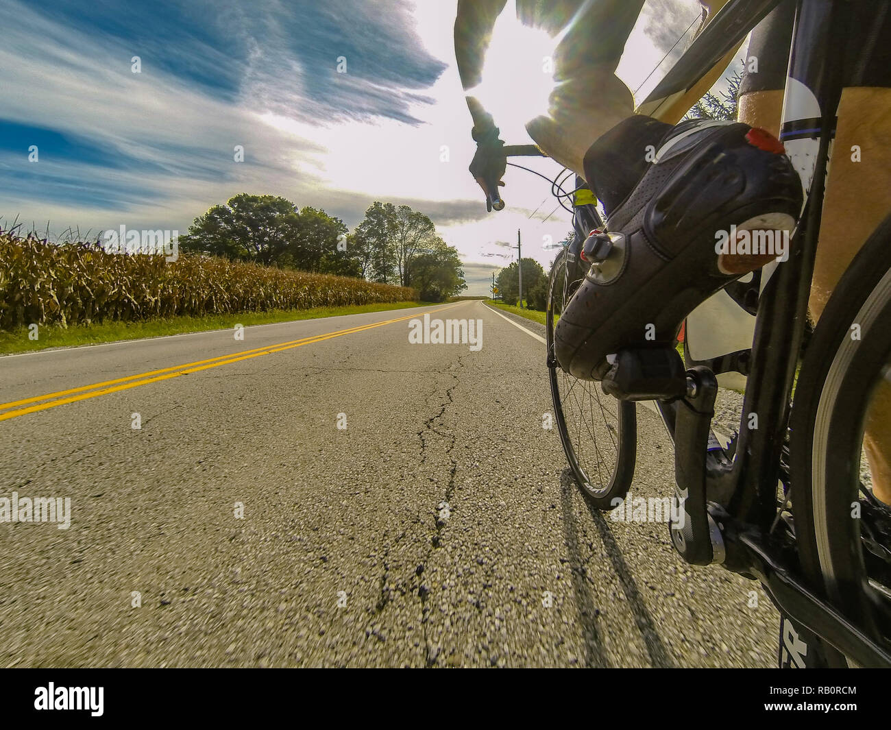 A male cyclist passing cornfields in Ohio on a road racing bike in the morning DCIM101GOPRO Stock Photo