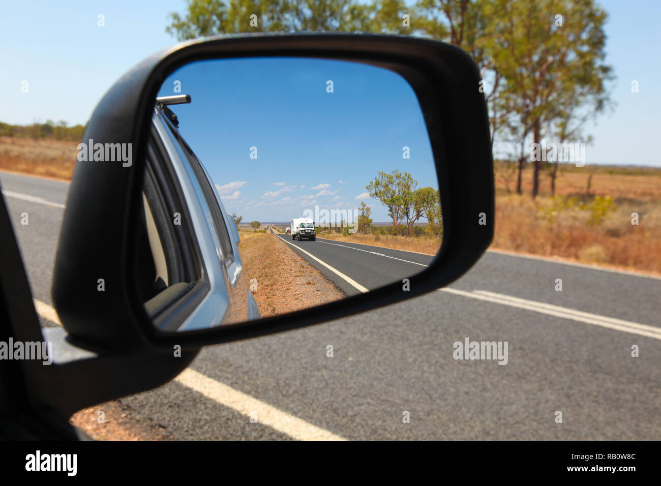 View in the side mirror on the Carnarvon Highway in Central Queensland Australia. 4WD vehicle towing caravan and outback Australian landscape Stock Photo