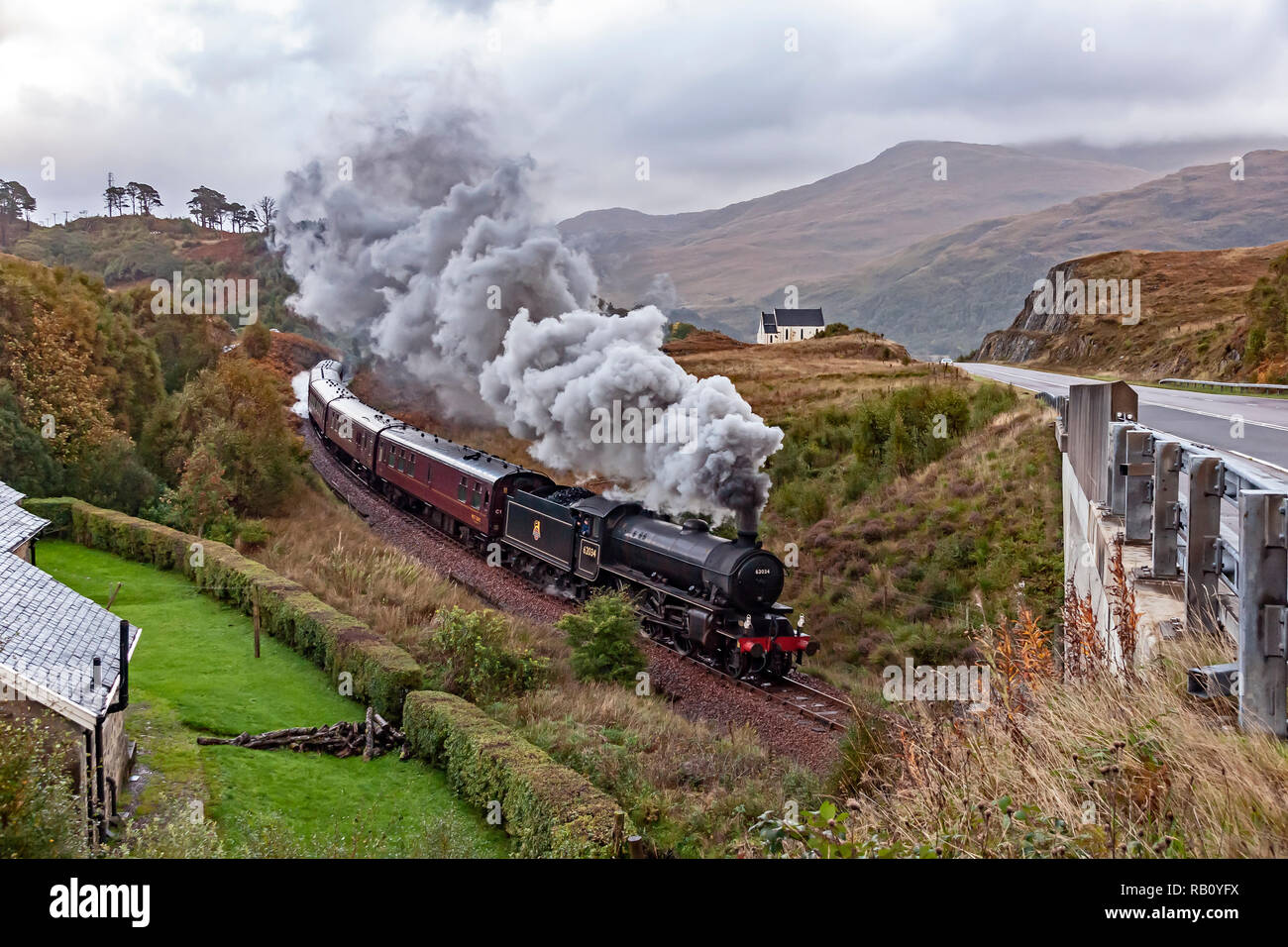 K1 steam engine No. 62034 pulls the Jacobite steam train past the famous church at Polnish at A830 en route to Mallaig from Fort William in Scotland Stock Photo