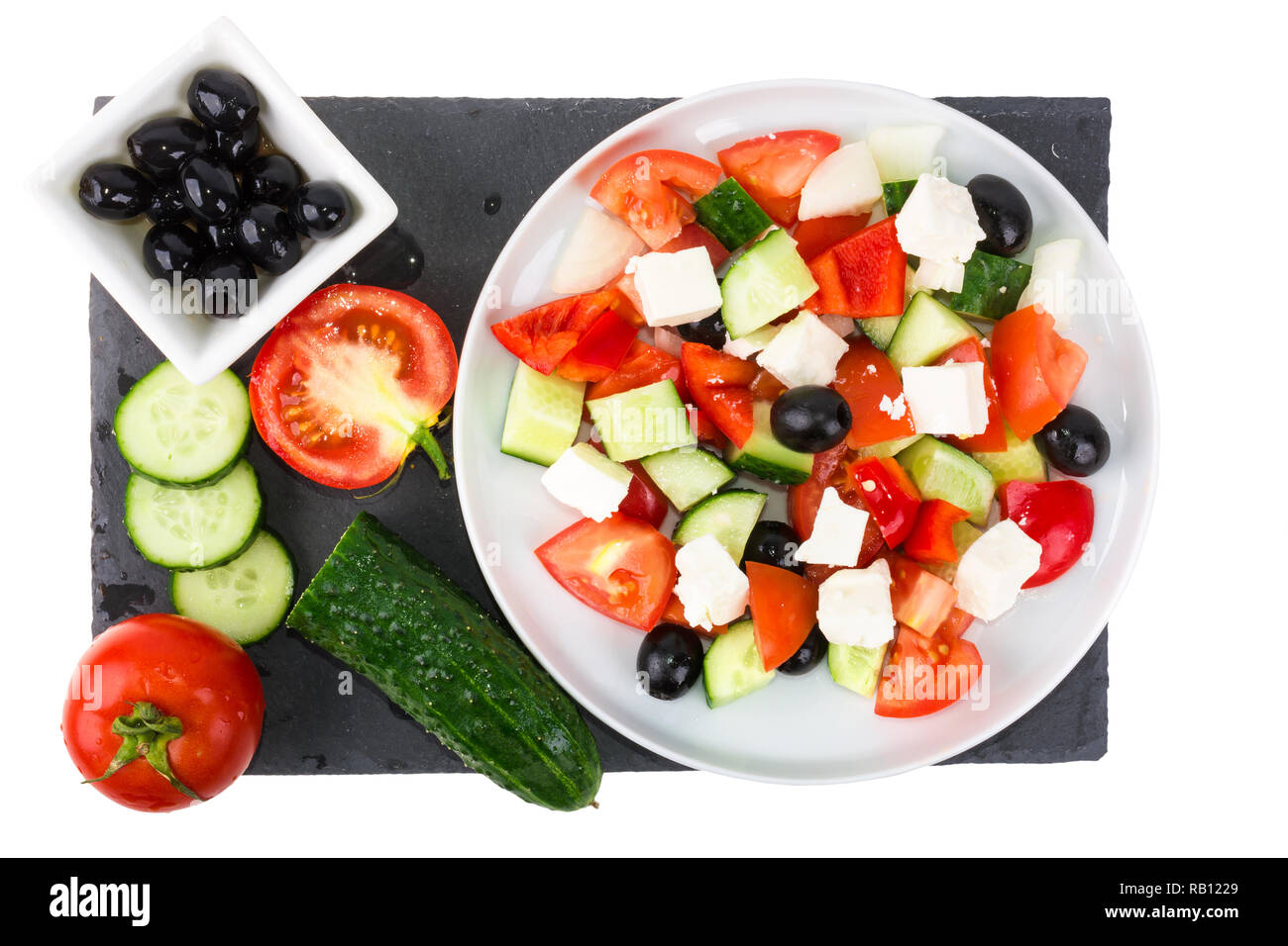 Greek salad with fresh vegetables, feta cheese and black olives in a plate with ingredients isolated on white background. top view Stock Photo