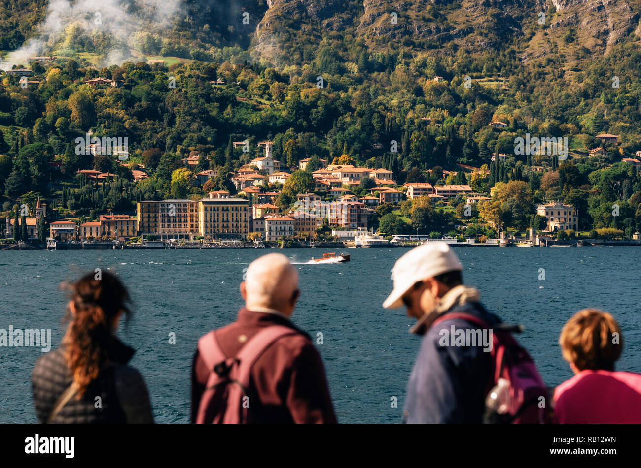 Cadenabbia, Italy - October 7, 2017: Tourists watch how boat moves against Cadenabbia town with buildings and hotels, coast of beautiful Como lake, It Stock Photo