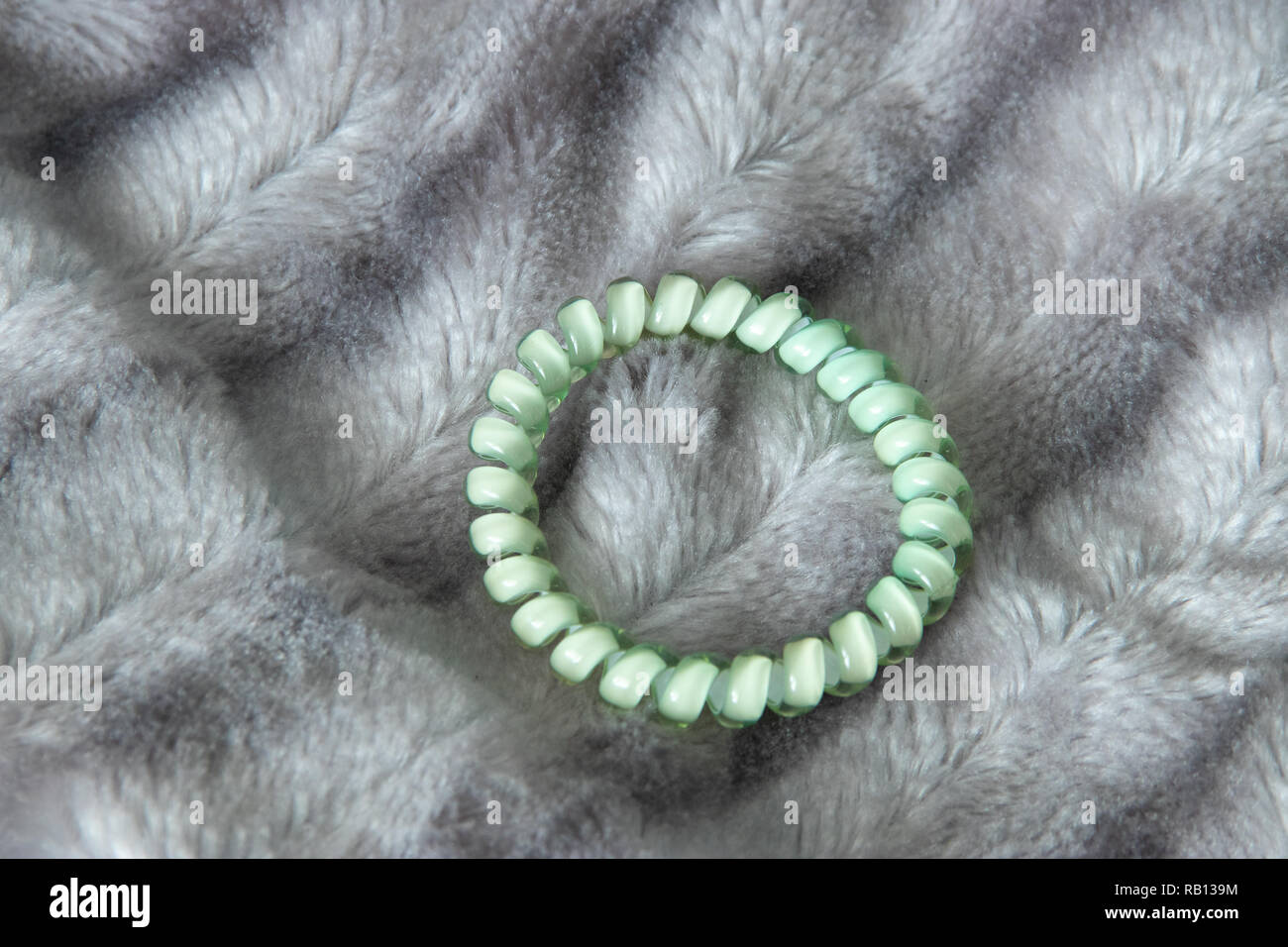 One light green blue scrunchy hair tie elastic spring on the silver gray fluffy faux fur blanket background Stock Photo