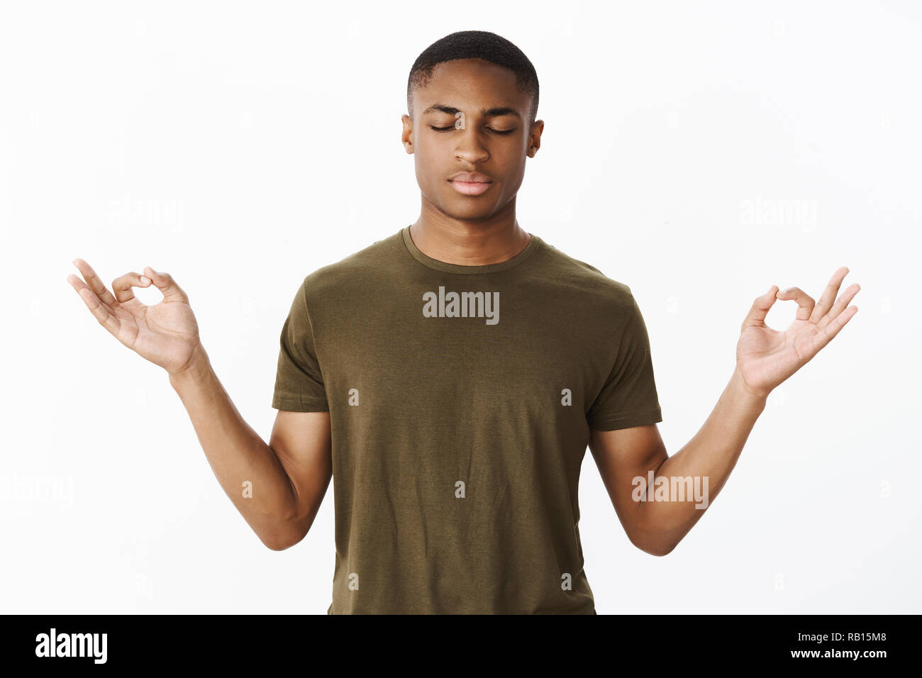 Studio shot of calm and peaceful young african american sportsman standing in lotus pose searching nirvana and patience with closed eyes and determined look practicing yoga or meditation Stock Photo